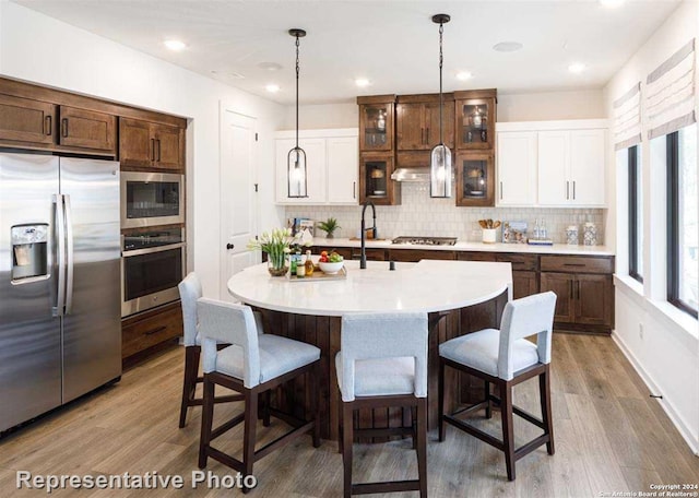 kitchen featuring stainless steel appliances, tasteful backsplash, decorative light fixtures, and hardwood / wood-style flooring