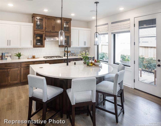 kitchen with white cabinets, an island with sink, hanging light fixtures, dark hardwood / wood-style flooring, and decorative backsplash