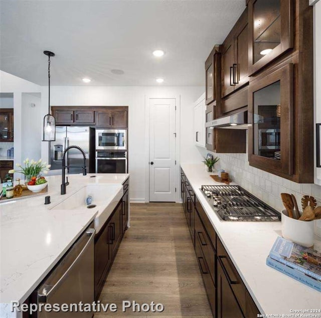 kitchen featuring stainless steel appliances, tasteful backsplash, dark wood-type flooring, hanging light fixtures, and dark brown cabinets