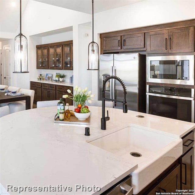 kitchen featuring lofted ceiling, light stone counters, sink, hanging light fixtures, and appliances with stainless steel finishes