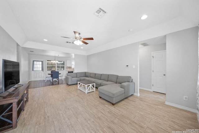 living room featuring ceiling fan with notable chandelier and light wood-type flooring