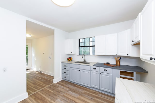 kitchen with light hardwood / wood-style floors, white cabinets, tasteful backsplash, and sink