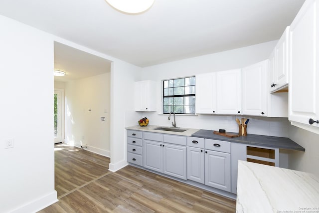 kitchen featuring decorative backsplash, white cabinets, a sink, baseboards, and light wood finished floors