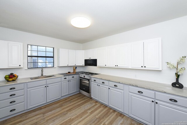 kitchen with high end stove, a sink, black microwave, gray cabinetry, and light wood-type flooring