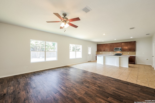 kitchen with ceiling fan, a kitchen island, backsplash, appliances with stainless steel finishes, and light hardwood / wood-style floors