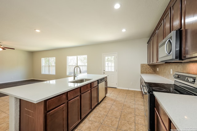 kitchen with a kitchen island with sink, stainless steel appliances, tasteful backsplash, sink, and light tile patterned floors