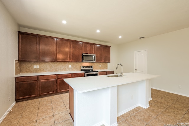 kitchen featuring sink, appliances with stainless steel finishes, a center island with sink, light tile patterned floors, and backsplash