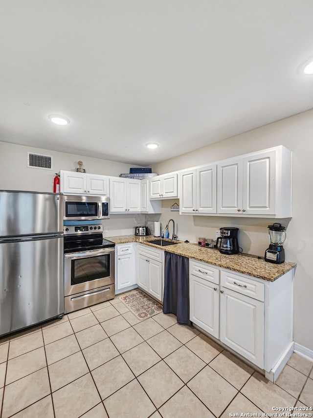 kitchen with light stone counters, stainless steel appliances, sink, white cabinetry, and light tile patterned floors