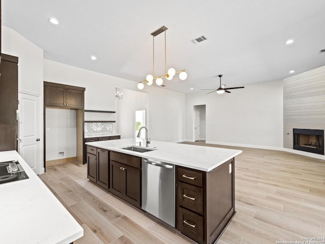 kitchen featuring sink, hanging light fixtures, a large fireplace, a center island with sink, and stainless steel dishwasher