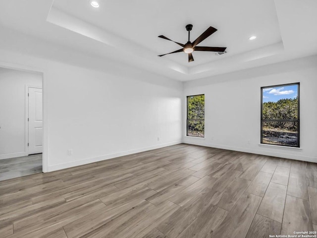 empty room featuring a raised ceiling, ceiling fan, and light hardwood / wood-style floors