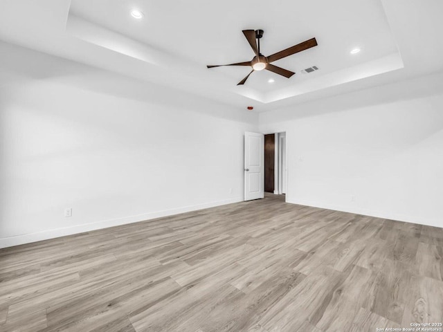 unfurnished room with ceiling fan, a raised ceiling, and light wood-type flooring