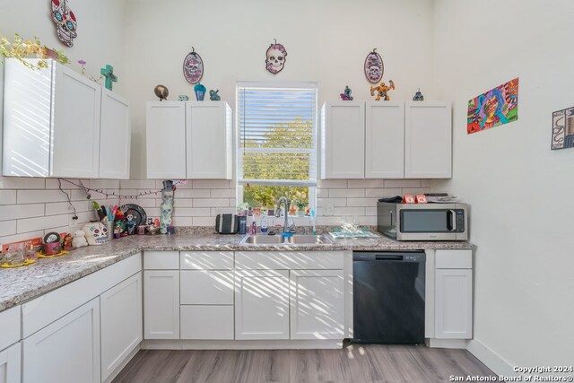 kitchen featuring light stone counters, white cabinets, sink, black dishwasher, and light hardwood / wood-style floors