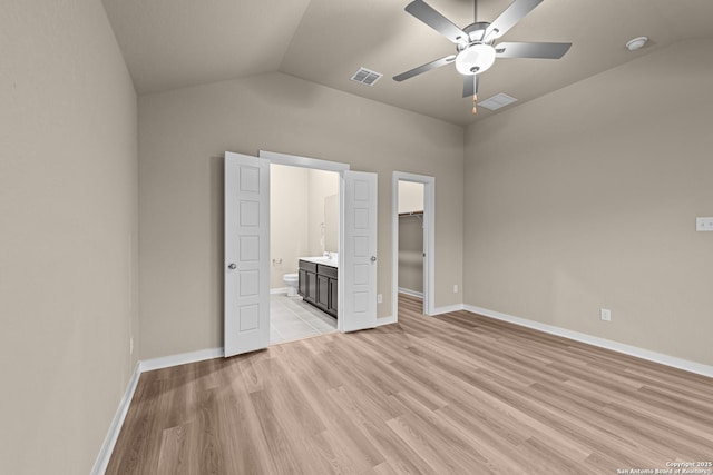 unfurnished bedroom featuring vaulted ceiling, connected bathroom, a walk in closet, ceiling fan, and light hardwood / wood-style flooring