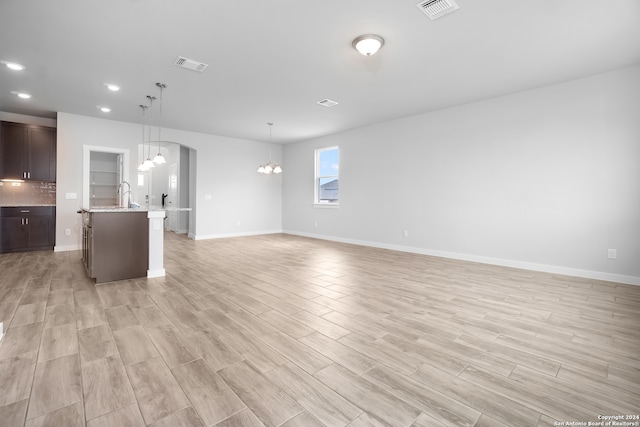 unfurnished living room featuring a notable chandelier, light hardwood / wood-style flooring, and sink