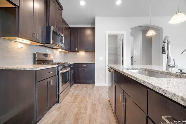 kitchen featuring pendant lighting, dark brown cabinetry, sink, light stone countertops, and appliances with stainless steel finishes