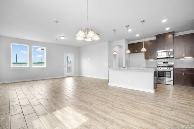 kitchen featuring light wood-type flooring, light stone countertops, a notable chandelier, appliances with stainless steel finishes, and decorative light fixtures