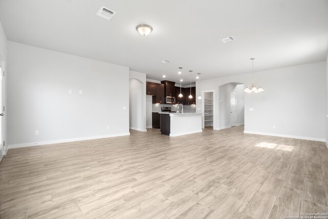 unfurnished living room featuring an inviting chandelier, light wood-type flooring, and sink