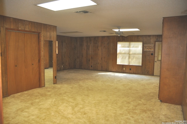 unfurnished room with wooden walls, ceiling fan, and light colored carpet