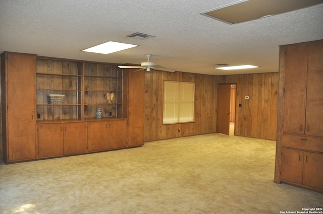 unfurnished room with wooden walls, light colored carpet, a textured ceiling, and ceiling fan