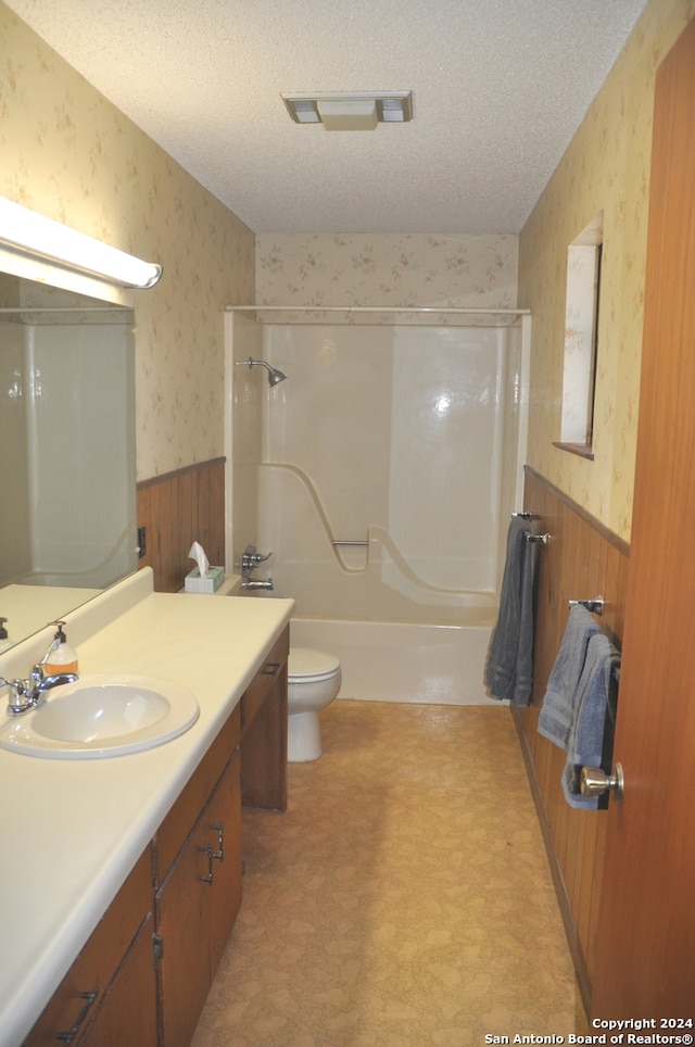 full bathroom with wood walls, toilet, vanity, shower / tub combination, and a textured ceiling