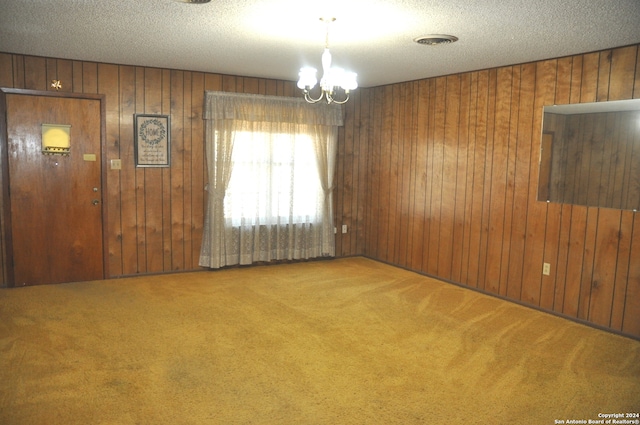 spare room with an inviting chandelier, wooden walls, a textured ceiling, and carpet