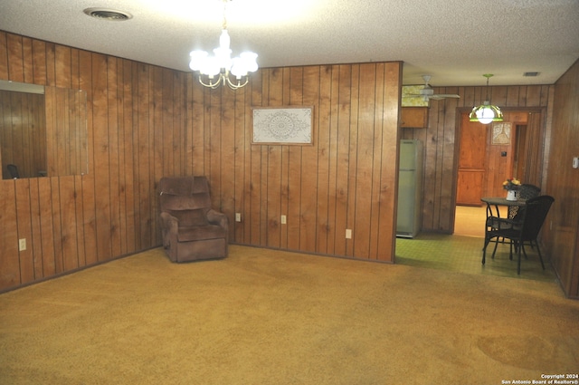 unfurnished room featuring a textured ceiling, a notable chandelier, wood walls, and carpet