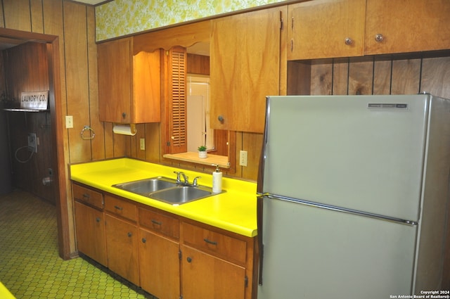 kitchen featuring stainless steel fridge, wooden walls, and sink