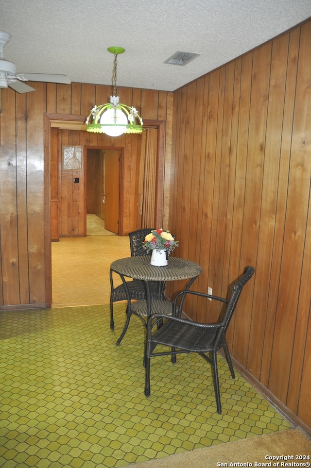 dining room with a textured ceiling, ceiling fan, wood walls, and light colored carpet