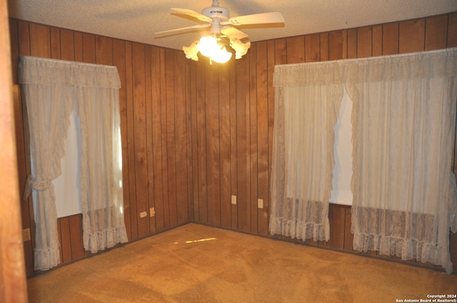 empty room featuring a textured ceiling, wooden walls, ceiling fan, and carpet flooring