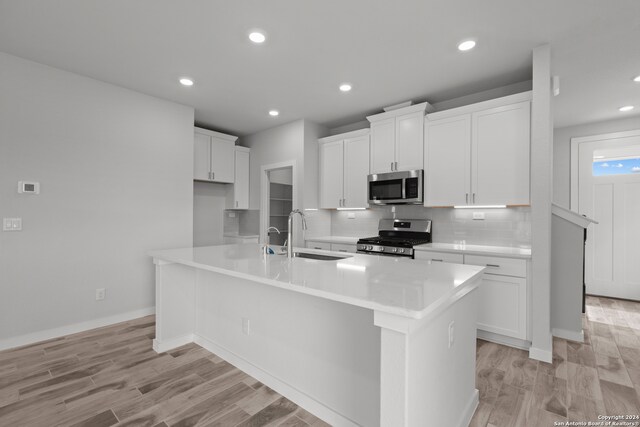 kitchen with white cabinets, sink, a center island with sink, stainless steel appliances, and light hardwood / wood-style floors