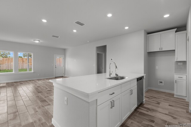 kitchen featuring a kitchen island with sink, light wood-type flooring, sink, stainless steel dishwasher, and white cabinetry