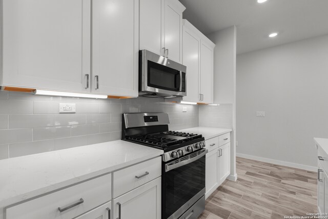 kitchen featuring backsplash, white cabinetry, appliances with stainless steel finishes, light stone countertops, and light hardwood / wood-style floors