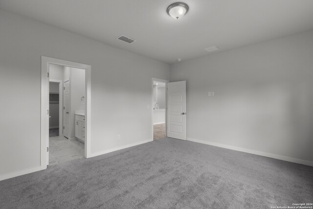 unfurnished bedroom with a closet, light colored carpet, a walk in closet, and ensuite bathroom