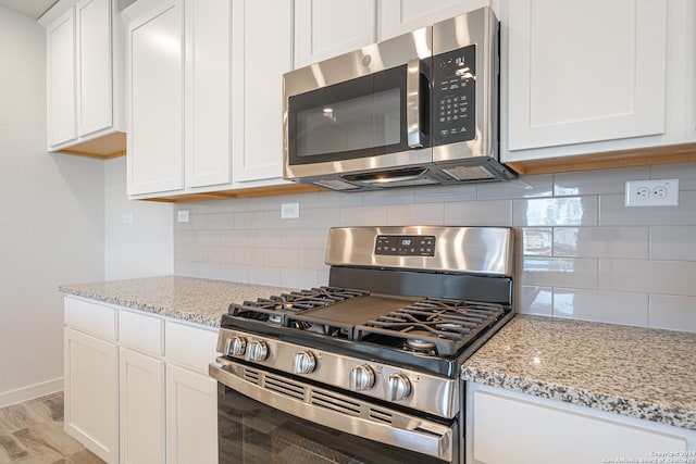 kitchen with light hardwood / wood-style flooring, decorative backsplash, light stone countertops, appliances with stainless steel finishes, and white cabinetry