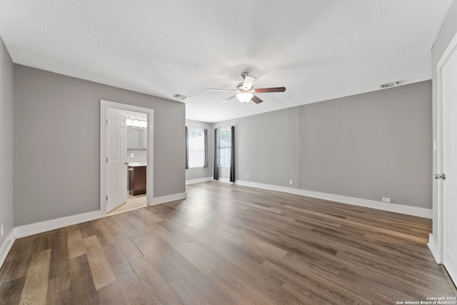 unfurnished bedroom featuring hardwood / wood-style flooring, ensuite bath, ceiling fan, and a textured ceiling