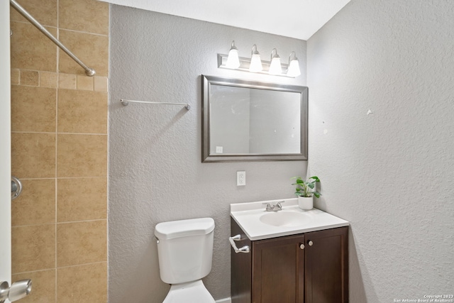 bathroom with tiled shower, vanity, and toilet