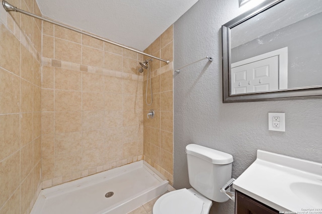 bathroom with a tile shower, vanity, toilet, and a textured ceiling