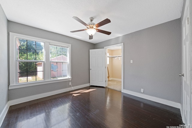 unfurnished bedroom with a spacious closet, ceiling fan, a closet, dark hardwood / wood-style flooring, and a textured ceiling