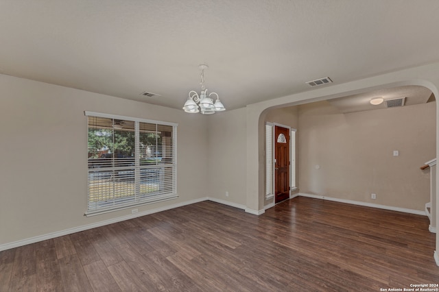 spare room featuring dark wood-type flooring and a chandelier