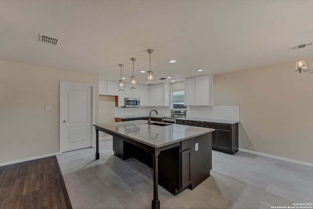 kitchen featuring appliances with stainless steel finishes, light stone countertops, white cabinets, and a kitchen island with sink