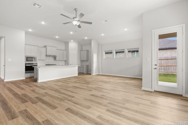 kitchen featuring built in microwave, stainless steel oven, ceiling fan, light hardwood / wood-style floors, and a center island with sink