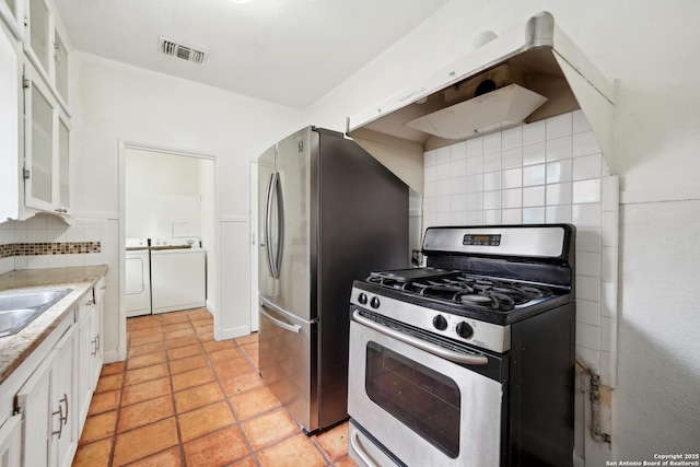 kitchen featuring appliances with stainless steel finishes, tasteful backsplash, extractor fan, washer and clothes dryer, and white cabinets