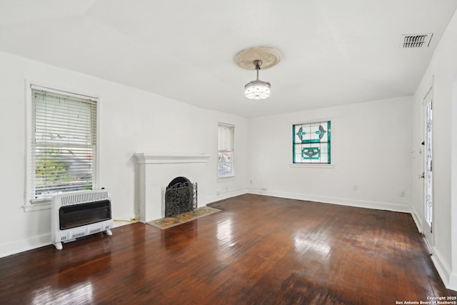 unfurnished living room featuring dark wood-type flooring, heating unit, and a healthy amount of sunlight