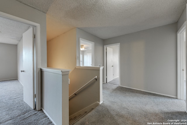 hall with a textured ceiling and light colored carpet