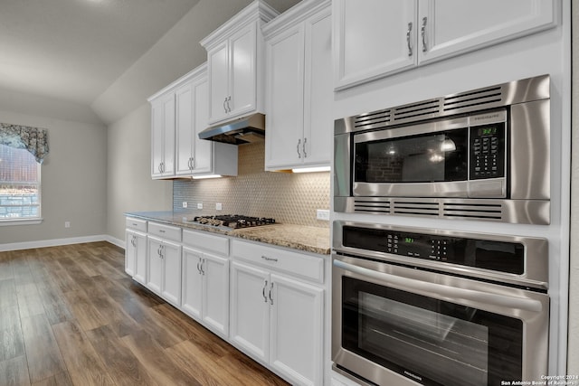 kitchen featuring backsplash, white cabinets, dark hardwood / wood-style floors, appliances with stainless steel finishes, and light stone counters