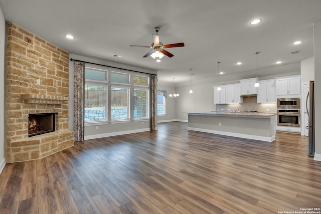 unfurnished living room featuring dark hardwood / wood-style floors, a stone fireplace, and ceiling fan with notable chandelier