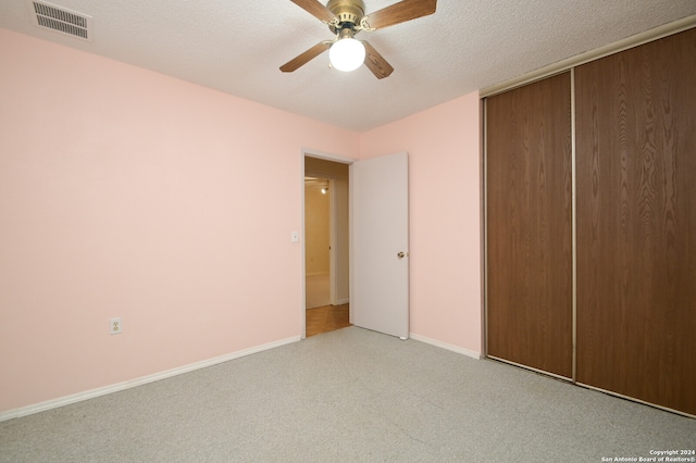 unfurnished bedroom featuring ceiling fan, light colored carpet, a textured ceiling, and a closet