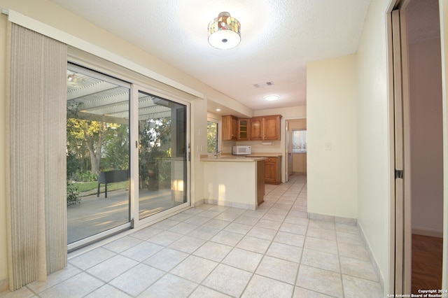 kitchen with light tile patterned flooring, kitchen peninsula, and a textured ceiling