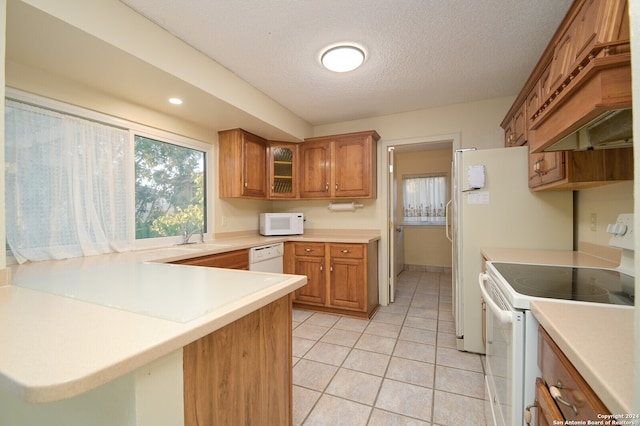 kitchen featuring white appliances, kitchen peninsula, premium range hood, light tile patterned floors, and a textured ceiling