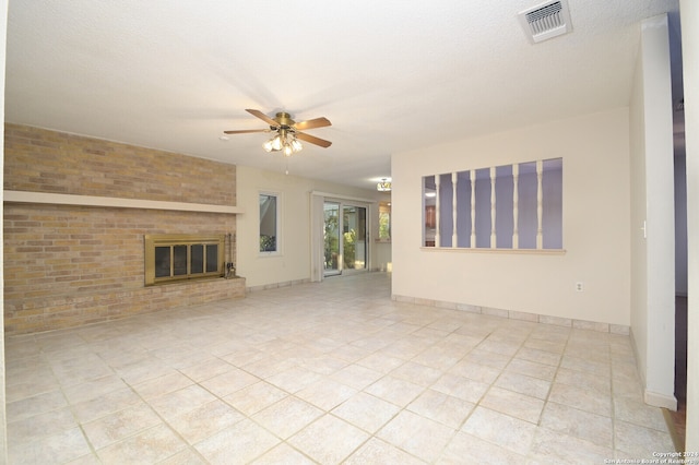 unfurnished living room with ceiling fan, light tile patterned flooring, brick wall, a textured ceiling, and a fireplace